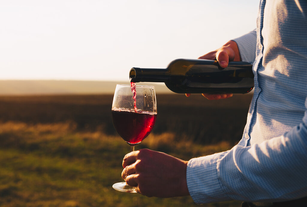 persona-que-vierte-vino-tinto-en-un-vaso-al-atardecer